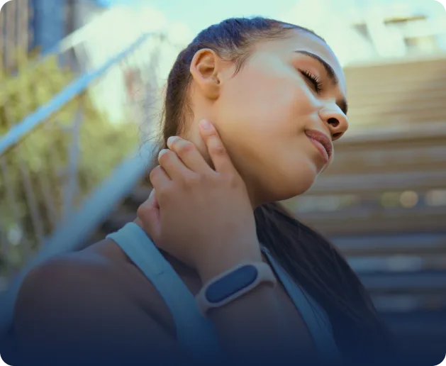 Woman touching her neck and thyroid area while looking upward outdoors